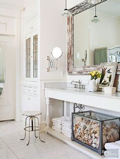 A vintage milking stool and seashell-stuffed aquarium highlight this bathroom&#39;s mix of country and cottage styles. To get a similar look, start with a white backdrop that will show off chipped patinas and beachcombed treasures. Install vintage-looking light fixtures, faucets, mirrors, and hardware to instill an aged appearance.??/
