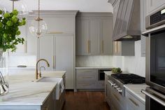 Gold and gray kitchen features creamy gray cabinets adorned with long brushed???