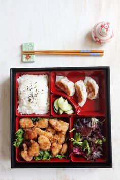 Japanese Fried Chicken Bento with steamed rice and sesame seeds, pickled cucumbers, salad and Gyoza. 